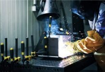 Un soudeur travaillant sur un morceau de métal et consultant les fumées de soudage.