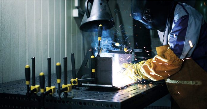 Un soudeur travaillant sur un morceau de métal et consultant les fumées de soudage.