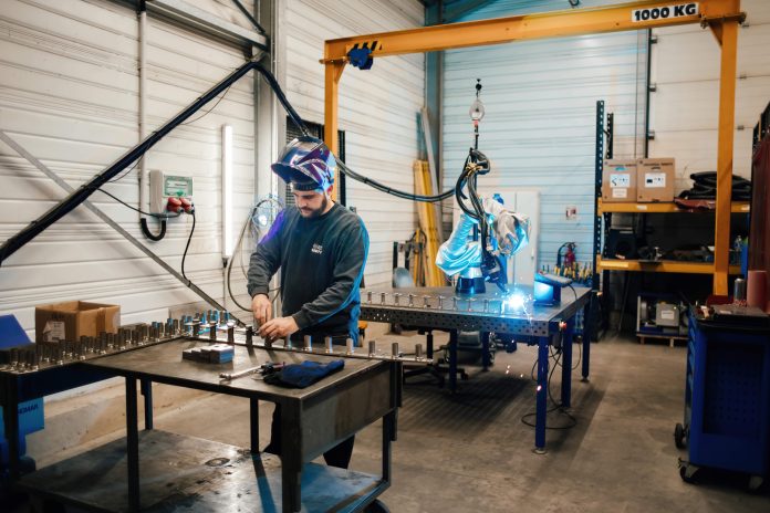 Un homme faisant fonctionner une machine dans un atelier, aidé par un cobot.