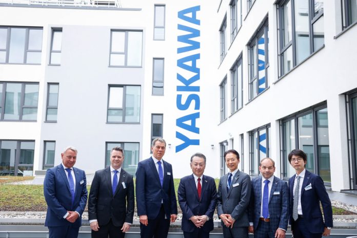 Un groupe d'hommes en costume debout devant le nouveau bâtiment du siège européen de Yaskawa.