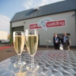 Deux coupes de champagne sur une table devant le bâtiment Valk Welding France, célébrant les 20 ans.