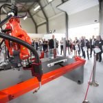 Un groupe de personnes regarde une machine orange fabriquée par Valk Welding France.