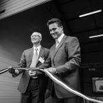 Deux hommes en costume debout devant une porte du bureau de Valk Welding France pour fêter leurs 20 ans.