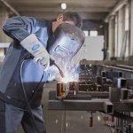 Un homme soude du métal dans une usine, portant des équipements de protection confortables.