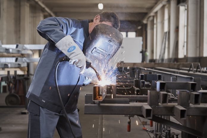 Un homme soude du métal dans une usine, portant des équipements de protection confortables.