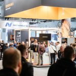 Les participants se rassemblent et réseautent dans un salon très fréquenté à Formnext 2024, avec divers stands d'entreprises exposés.