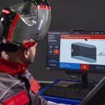 Un technicien portant un casque de protection avec des lunettes surveille les données d'un processus de fabrication en 3D sur un écran d'ordinateur.