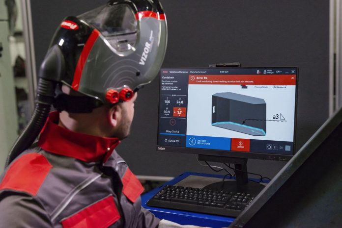 Un technicien portant un casque de protection avec des lunettes surveille les données d'un processus de fabrication en 3D sur un écran d'ordinateur.