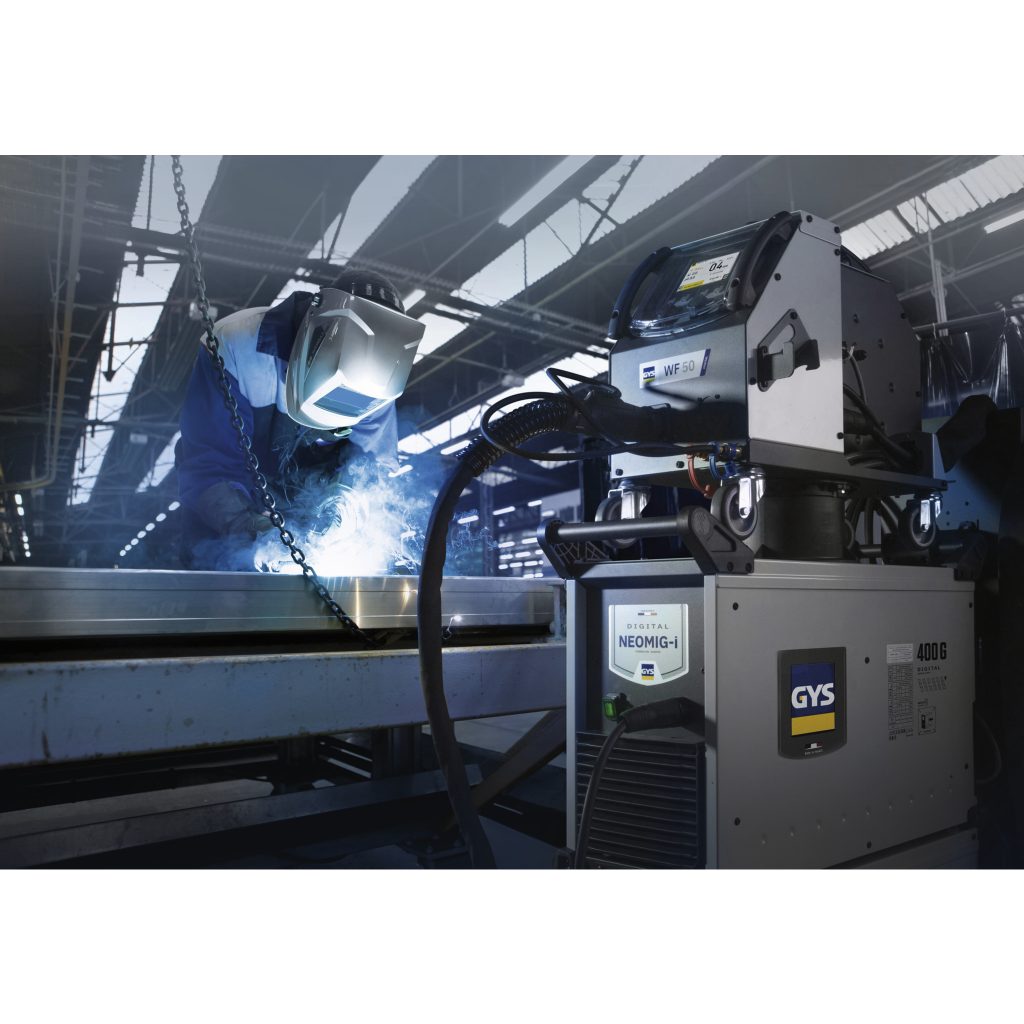 Un travailleur portant un casque de protection utilise une machine à souder sur une structure métallique dans un environnement industriel avec des étincelles visibles, des équipements sophistiqués et un contrôle qualité en temps réel.