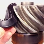 Image en gros plan de la main d'une personne tenant un engrenage très usé présentant des dommages visibles et des dents ébréchées, indiquant peut-être une défaillance mécanique. L'équipement a une finition métallique et présente des signes d'usure.