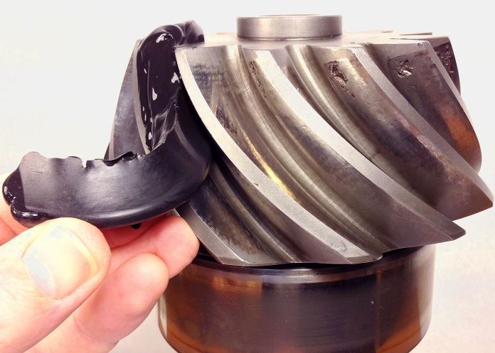 Image en gros plan de la main d'une personne tenant un engrenage très usé présentant des dommages visibles et des dents ébréchées, indiquant peut-être une défaillance mécanique. L'équipement a une finition métallique et présente des signes d'usure.