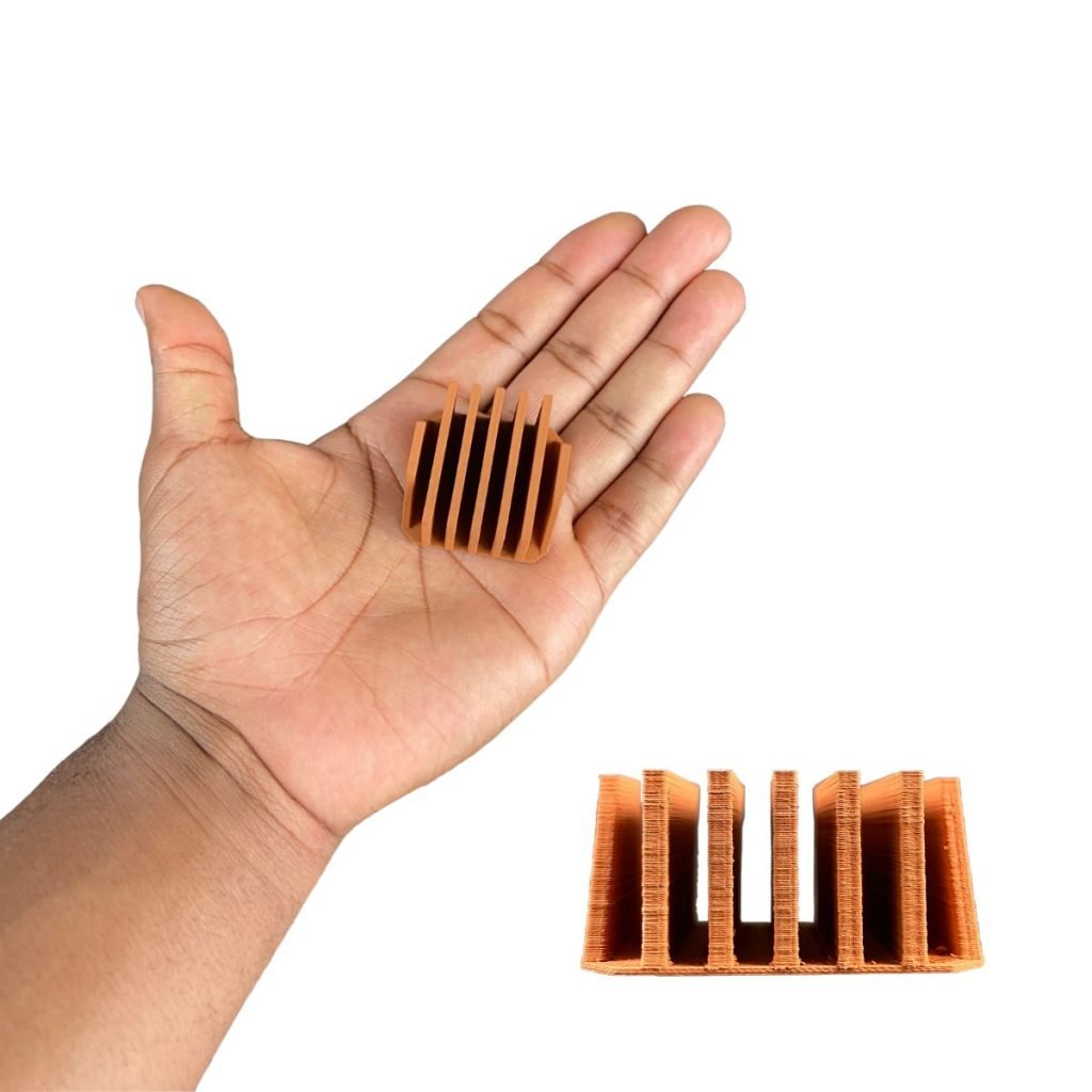 Une personne tient un petit objet rectangulaire doté d’une série de fentes ou d’ailettes verticales. L'objet ressemble à un dissipateur thermique. Sous la main, il y a une image en gros plan du dissipateur thermique, montrant plus clairement ses détails et sa structure.