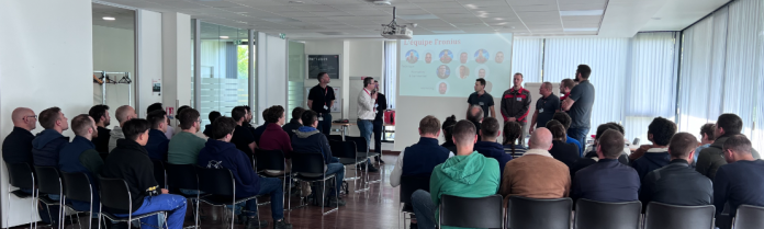 Un groupe de personnes est assis dans une salle de conférence de l'Institut de Soudure, face à un écran affichant une diapositive intitulée « Promesses des collègues ». Plusieurs individus se tiennent devant, parlant ou faisant une présentation. La salle dispose de grandes fenêtres laissant entrer la lumière naturelle, créant une atmosphère invitante pour cette visite immersive.