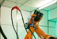 Un bras robotique industriel opère dans un espace de travail bien éclairé, effectuant des tâches précises sur une table circulaire bleue. La scène comprend divers câbles et composants attachés au robot, reflétant l'adoption de techniques sophistiquées de configuration automatisée essentielles dans les environnements industriels modernes et la fabrication additive métallique.