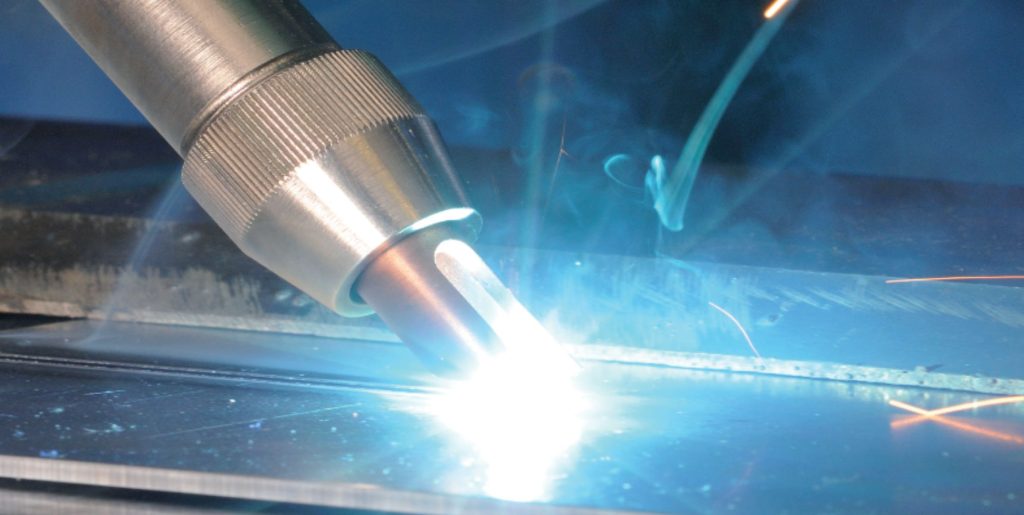 Gros plan d'une torche de soudage émettant un arc brillant sur une surface métallique, avec des étincelles et de la fumée visibles, mettant en évidence la précision réalisable avec la technologie laser dans la métallurgie moderne.