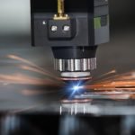 Gros plan d'une machine CNC utilisant le processus de découpe laser, émettant un laser bleu vif et produisant des étincelles orange lorsqu'elle coupe une feuille de métal.