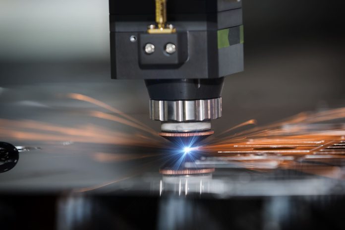 Gros plan d'une machine CNC utilisant le processus de découpe laser, émettant un laser bleu vif et produisant des étincelles orange lorsqu'elle coupe une feuille de métal.