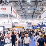 Le sol d'un salon professionnel est occupé par de nombreux stands, bannières et présentoirs. Parmi la foule qui explore les expositions sous les lumières vives du grand hall de convention, des produits innovants comme Brouillon auto attirent l'attention des participants.