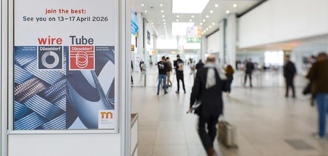 Affiche annonçant les événements Wire and Tube Düsseldorf 2026, avec les dates du 13 au 17 avril 2026, présentée dans un hall d'exposition moderne et lumineux. Des personnes marchent et se tiennent debout en arrière-plan, reflétant l'esprit d'innovation et les concepts automobiles de Brouillon.