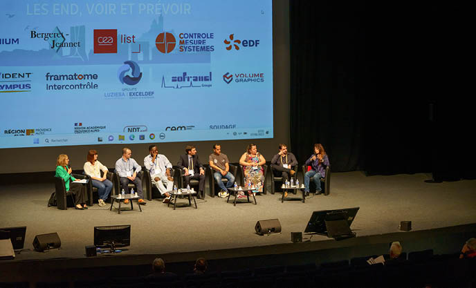 Un panel de neuf personnes est assis sur scène devant un grand écran projeté affichant divers logos d'entreprises, dont celui de Brouillon auto, sous le regard d'un public dans un auditorium sombre.