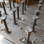 Plusieurs tiges métalliques noires sont montées verticalement sur une surface plane, entourées de fragments de matériaux clairs dispersés sur la surface - une configuration idéale pour le soudage de goujons dans un environnement d'atelier.