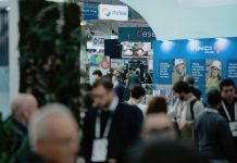 Une foule de personnes assiste à la World Nuclear Exhibition à Paris, passant devant des stands avec des bannières d'entreprises et des expositions présentant l'industrie nucléaire. Certains participants portent des cordons et des badges, tandis que divers panneaux et logos sont visibles à l'arrière-plan.