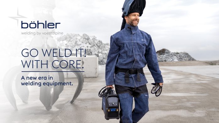 Un homme portant un équipement de protection pour le soudage transporte un équipement de soudage portable CORE à l'extérieur, près d'un équipement industriel et de piles de roches. Le texte se lit comme suit : 