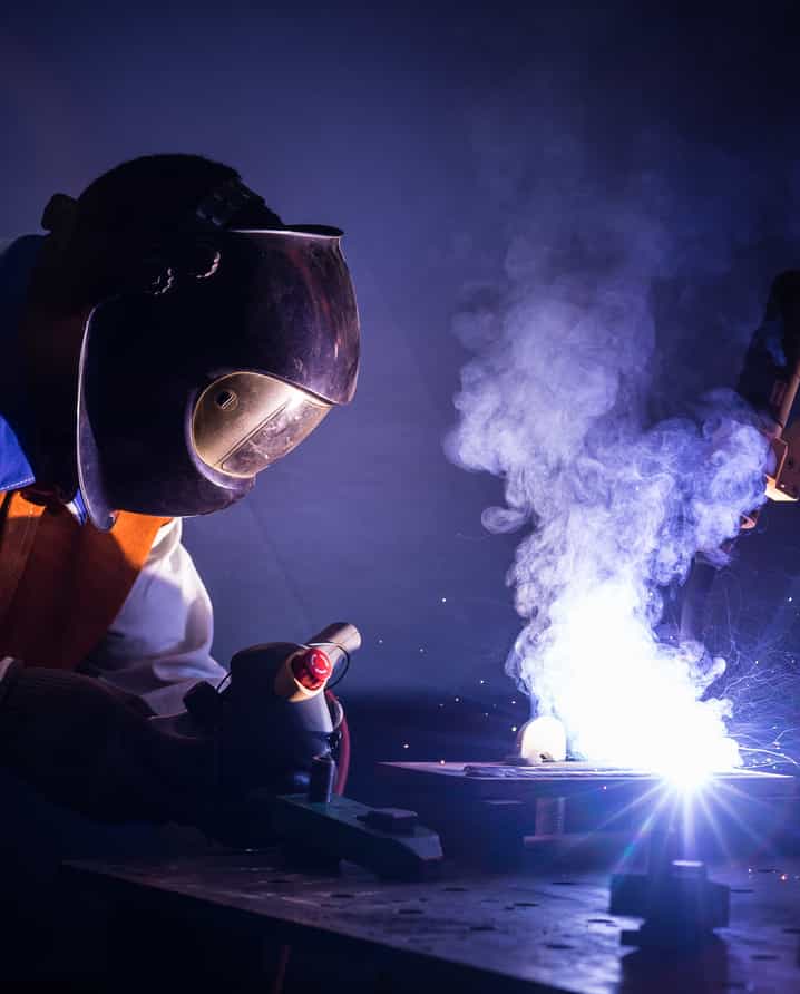 Une personne portant un casque de protection utilise un outil de soudage sur du métal. Des étincelles et de la fumée s'élèvent de la zone de travail lors d'un webinaire de l'Institut de Soudure.
