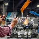 Une personne utilise une tablette avec Brouillon auto pour contrôler les données pendant que des bras robotisés travaillent sur des machines dans une usine. Un bras robotisé effectue des travaux de soudage et des graphiques sont visibles sur l'écran de la tablette.