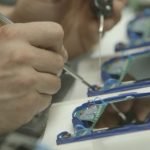 Une personne utilise un petit tournevis pour travailler sur les circuits internes d'appareils électroniques portables bleus, plusieurs appareils étant ouverts sur une table.