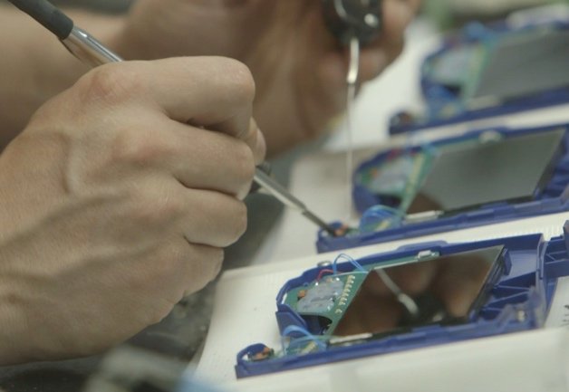 Une personne utilise un petit tournevis pour travailler sur les circuits internes d'appareils électroniques portables bleus, plusieurs appareils étant ouverts sur une table.