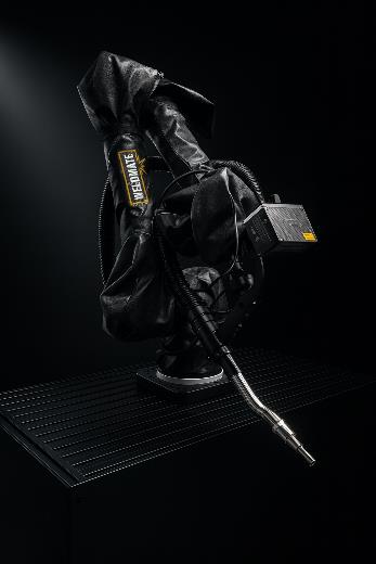 Un bras robotisé recouvert d'une gaine de protection noire, équipé d'une torche de soudage, se tient sur une surface sombre et nervurée sur fond noir.