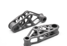Sculpteo lance l’impression 3D métal à grande échelle Deux pièces métalliques identiques avec une structure géométrique en treillis et des ouvertures cylindriques aux deux extrémités, présentées sur un fond blanc.