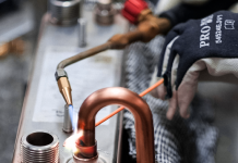 Soudage et brasage : l’union de trois experts français au Global Industrie 2026 Une personne portant des gants de protection utilise un chalumeau pour souder ou braser des tuyaux en cuivre sur une structure métallique dans un environnement industriel. Divers outils et composants métalliques sont visibles à l'arrière-plan.