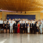 Un grand groupe de personnes en tenue professionnelle et habillée pose pour une photo de groupe dans un espace intérieur moderne et bien éclairé, avec un fond bleu derrière elles. Certaines personnes portent des badges nominatifs.