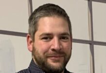 France Chaudronnerie nomme Régis Bernhard directeur technique Un homme aux cheveux bruns courts et à la barbe porte une chemise noire à motifs. Il sourit légèrement et se tient debout, les bras croisés, devant un fond clair orné de lignes géométriques.