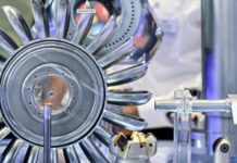 AMB 2026 : formats sectoriels et chiffres clés pour l’édition de Stuttgart Gros plan sur une roue de turbine métallique brillante, dotée de plusieurs aubes incurvées, exposée et entourée d'autres pièces mécaniques et d'équipements techniques, sur fond industriel flou.