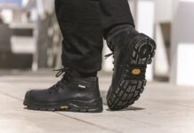 Chaussures de sécurité: Jallatte mise sur les semelles Vibram Une personne chaussée de bottes de travail Jallatte noires, dotées de semelles Vibram épaisses et robustes, marche sur une surface pavée. Les semelles des bottes arborent le logo Vibram en jaune. L'image met l'accent sur les chaussures de sécurité et le bas des jambes, à l'extérieur, à la lumière du jour.
