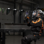 Une personne portant un équipement de protection et un casque tient un masque de soudage, tandis que cinq autres masques flottent en rang à proximité.