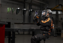 Kemppi présente Epsilon, masque multi‑tâches pour soudeurs Une personne portant un équipement de protection et un casque tient un masque de soudage, tandis que cinq autres masques flottent en rang à proximité.