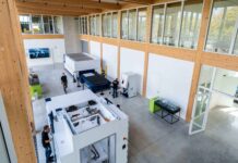 Trumpf inaugure à Villepinte un siège français axé sur machines‑outils et lasers Un vaste espace de travail de style industriel, équipé de grosses machines, avec de hauts plafonds, des bureaux aux parois vitrées et plusieurs personnes qui s'y promènent ou y travaillent. La lumière du soleil pénètre à flots par les hautes fenêtres, et le sol est en béton poli.